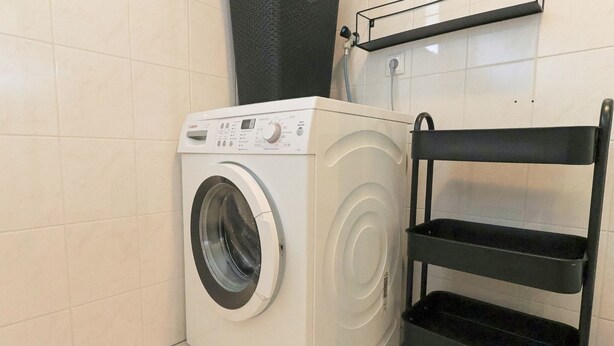 Una lavadora de carga frontal en un baño con paredes de azulejos y un estante negro.