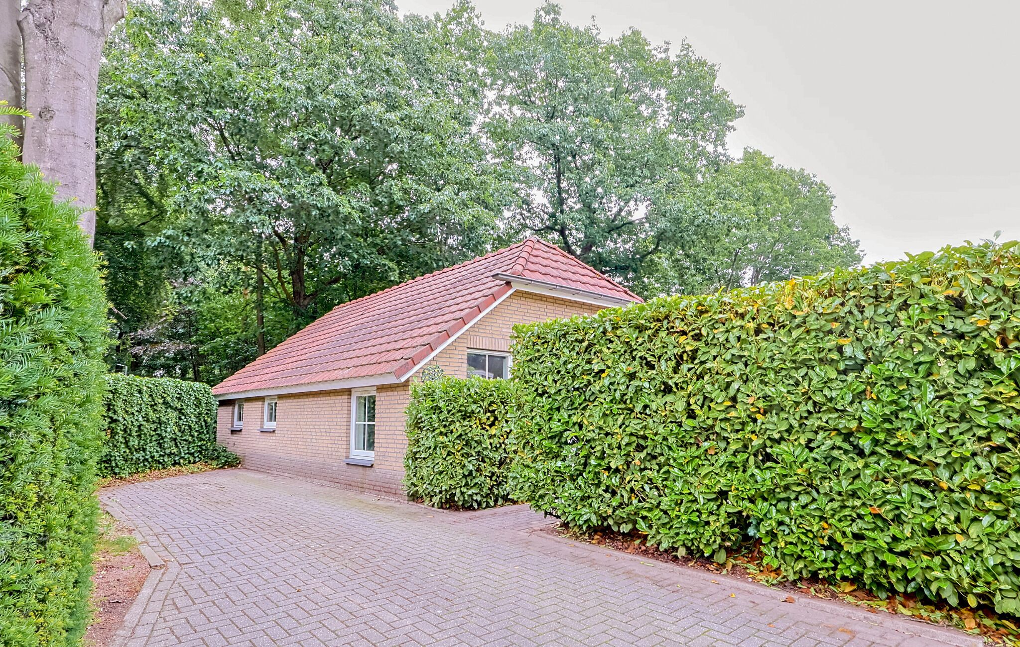 A single-story house with a red-tiled roof, a brick exterior, and a paved driveway.