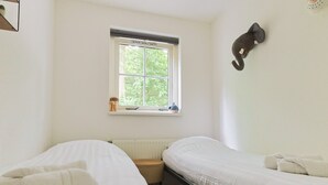 Una habitación con dos camas, una ventana con vistas a la vegetación, un radiador y un elefante decorativo colgado en la pared.