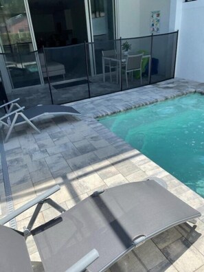 Une piscine dotée d’une paroi en verre, de chaises longues et d’un espace patio.