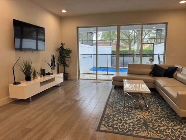 Un salon moderne comprenant un canapé, une table basse, un téléviseur et une grande fenêtre donnant sur une piscine.