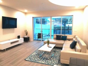 A modern living room with a sofa, coffee table, TV, and a balcony with outdoor furniture. - Modern Townhome with Private Splash Pool, Near Disney (Clermont)