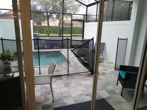 A glass-enclosed outdoor area with a pool, seating, and a view of the surrounding landscape. - Modern Townhome with Private Splash Pool, Near Disney (Clermont)