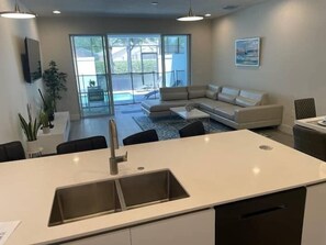 A modern kitchen with a large island, a dining area, and a living room with a sofa and a pool view. - Modern Townhome with Private Splash Pool, Near Disney (Clermont)