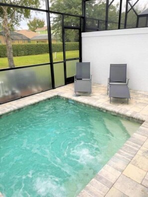 A swimming pool with two lounge chairs, surrounded by a tiled deck and large windows. - Modern Townhome with Private Splash Pool, Near Disney (Clermont)