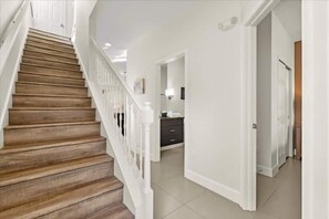 Eine Treppe mit Holzboden und weißen Geländern, die zu einem Raum mit einer weißen Tür und einem gefliesten Boden führt.