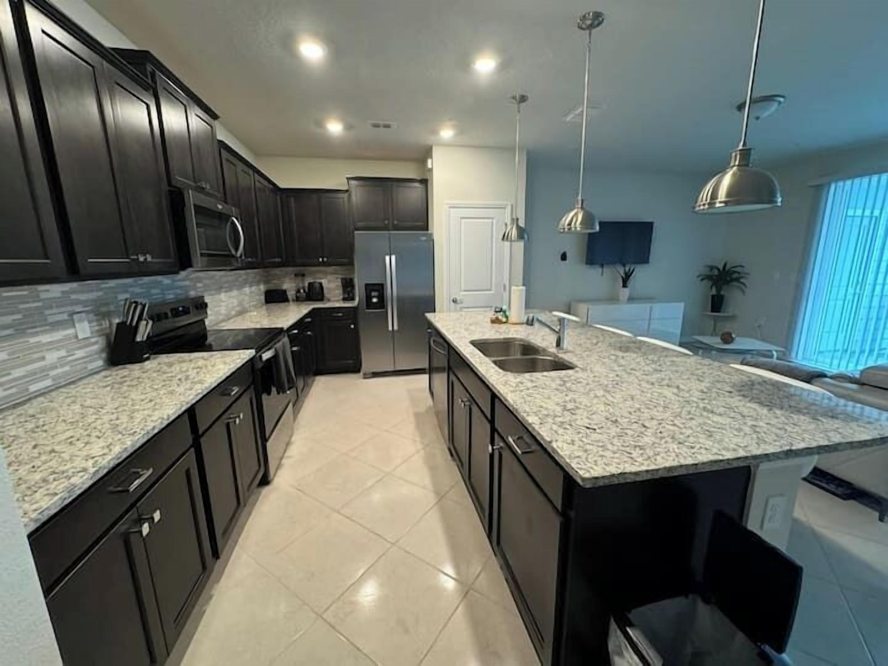 Una cocina moderna con gabinetes oscuros, encimeras de granito, electrodomésticos de acero inoxidable e iluminación colgante.