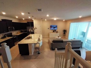 A modern kitchen with a central island, a dining area with a sofa, and a TV mounted on the wall. - Luxury 5BR Townhome with Private Pool at Windsor Cay Resort (Clermont, FL, USA)
