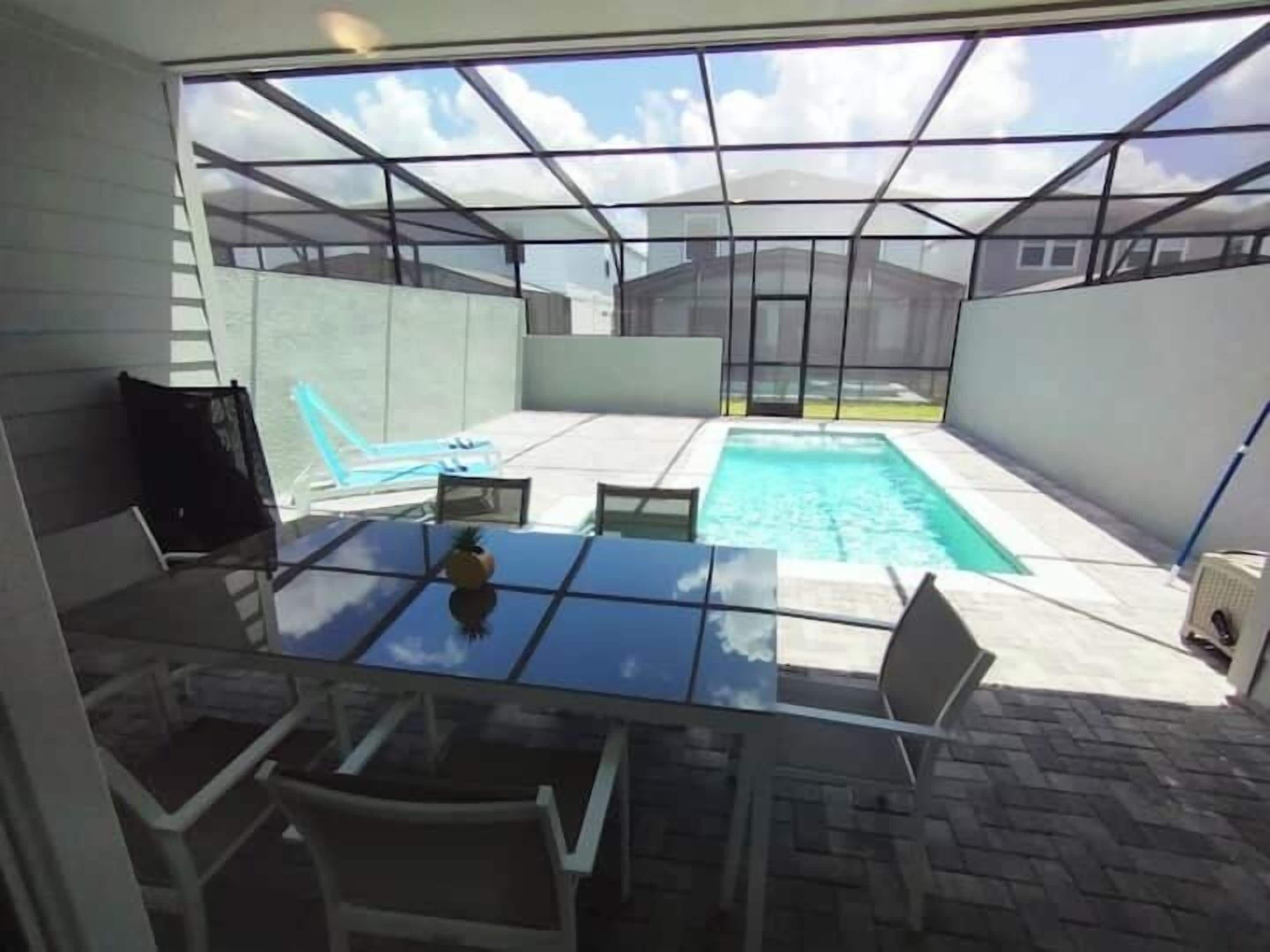 Ein von Glas umschlossener Patio mit Pool, Stühlen und Tisch.