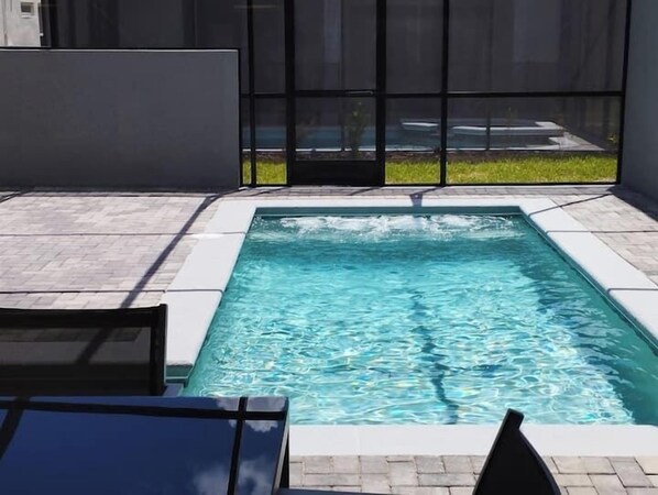 Et rektangulært pool med krystalklart vand, omgivet af en flisbelagt terrasse og et glashegn.