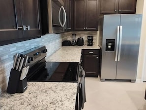 Eine moderne Küche mit dunklen Holzausziehtüren, einem Edelstahlkühlschrank, einem eingebauten Backofen und einer Arbeitsplatte aus Granit.