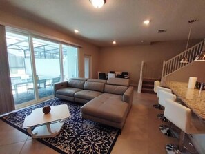 A modern living room with a sofa, a coffee table, and a dining area with bar stools. - Luxury 5BR Townhome with Private Pool at Windsor Cay Resort (Clermont, FL, USA)
