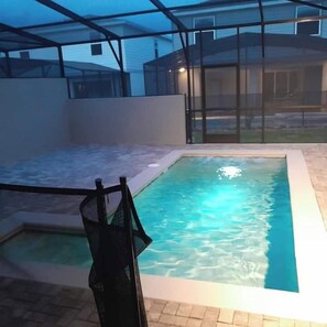 A swimming pool with a glass enclosure, surrounded by a paved area and a house in the background. - Luxury 5BR Townhome with Private Pool at Windsor Cay Resort (Clermont, FL, USA)