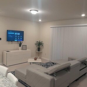 A modern living room with a sofa, a small table, a TV mounted on the wall, and a potted plant. - Luxury 5BR Townhome with Private Pool at Windsor Cay Resort (Clermont, FL, USA)