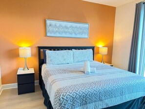 A neatly made bed with a patterned bedspread, two bedside lamps, a nightstand, and a framed abstract painting on the wall. - TR17430PA - Affordable Disney - Townhome 3Bd 3Ba Sleeps 6 Pond view (Clermont)