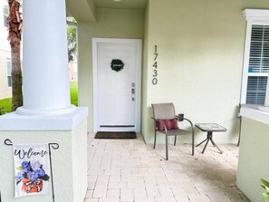 A house entrance with a white door, a number '17430' on the wall, a 'Welcome' sign, and a small table with a chair. - TR17430PA - Affordable Disney - Townhome 3Bd 3Ba Sleeps 6 Pond view (Clermont)