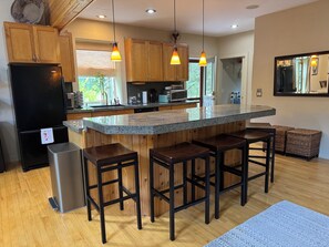 Eine moderne Küche mit Holzschränken, einem schwarzen Kühlschrank, einer Granitarbeitsplatte, hängenden Pendelleuchten und einer Bar mit Hockern.