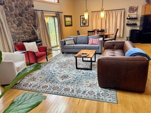 A living room with a stone wall, a gray sofa, a red chair, a brown leather couch, a wooden coffee table, and a patterned rug. - 4 Bedroom Sand Valley Golf Escape (Nekoosa)