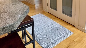 Um quarto com bancada de granito, uma cadeira de madeira, um tapete estampado, uma penteadeira com espelho e uma porta com painéis de vidro jateado.