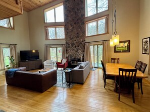 A spacious living area with a stone fireplace, a television, and a dining table with chairs. - 4 Bedroom Sand Valley Golf Escape (Nekoosa)
