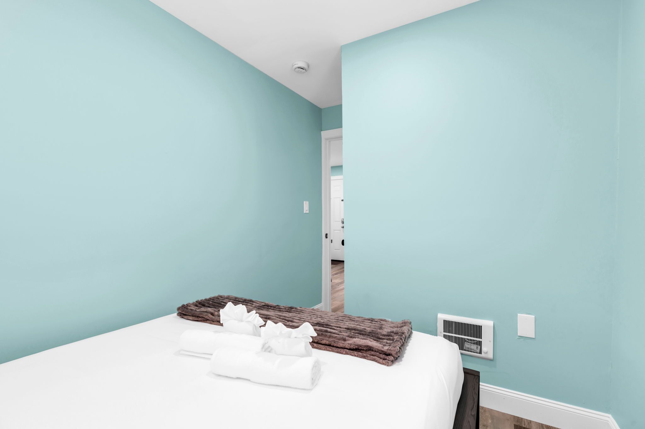 Une chambre avec des murs de couleur turquoise, un lit blanc, une couverture marron et une serviette blanche.