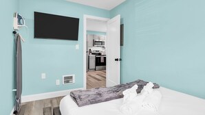 Un dormitorio con cama, televisor de pantalla plana, secador de pelo y vista hacia una zona de cocina.