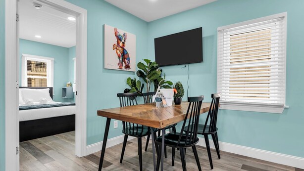 Un comedor con una mesa de madera, sillas negras, una planta en maceta y un cuadro en la pared.