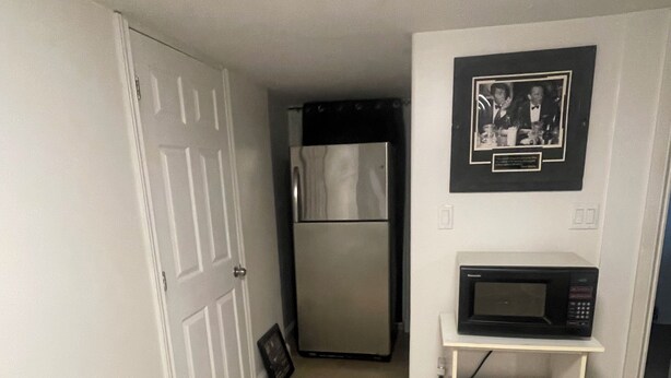 Un couloir avec une porte blanche, un réfrigérateur, un four à micro-ondes et un tableau encadré accroché au mur.