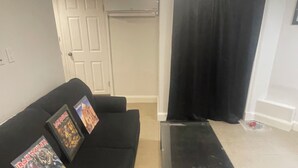 Un salon avec un canapé noir, une table basse en verre et un rideau noir.
