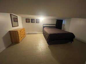Un dormitorio con cama, cómoda, cuadros en la pared y un calentador.