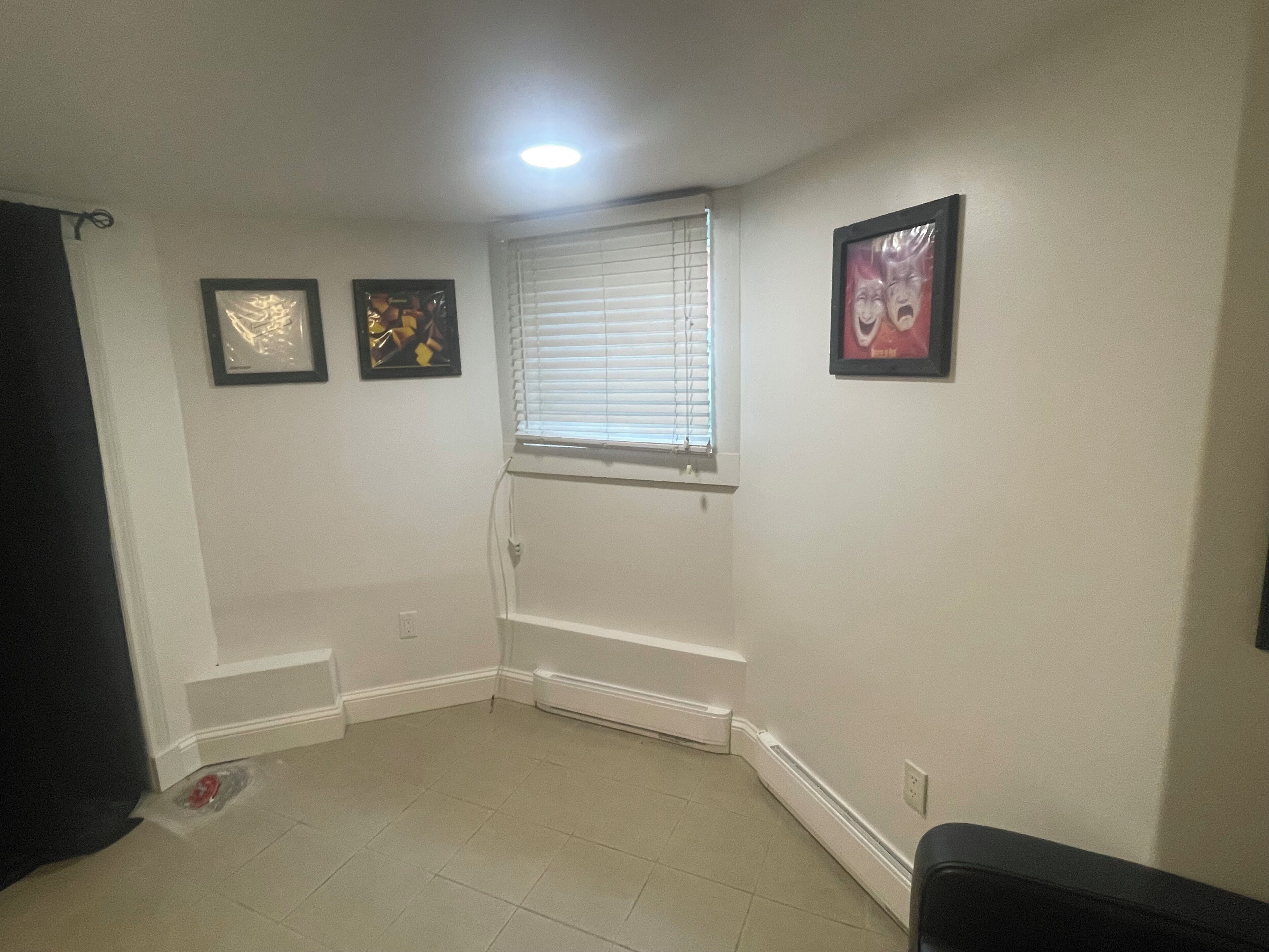 A room with a window, a radiator, and three framed pictures on the wall.