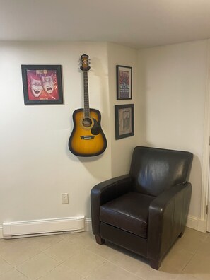 Una habitación con una guitarra, un sillón de cuero negro y cuadros en la pared.