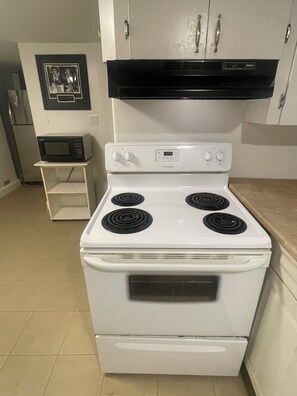 A kitchen with a white stove, a microwave on a small shelf, and a black range hood above the stove.