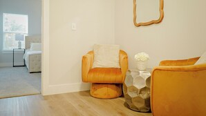 Una sala de estar moderna con un sofá, una butaca, una mesita con un florero y un espejo en la pared.