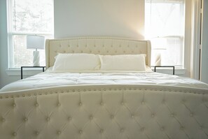Una cama con cabecera capitonada, ropa de cama blanca y dos mesitas de noche con lámparas.
