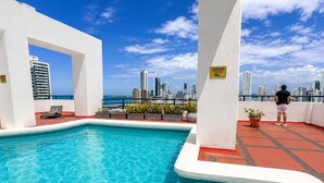 Piscina no terraço com vista para a cidade, placa indicando altura de 1,80 metros e uma pessoa perto da piscina.