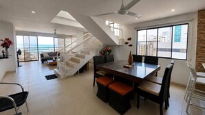 Uma sala de estar espaçosa com mesa de jantar, assentos confortáveis, escada e grandes janelas com vista.
