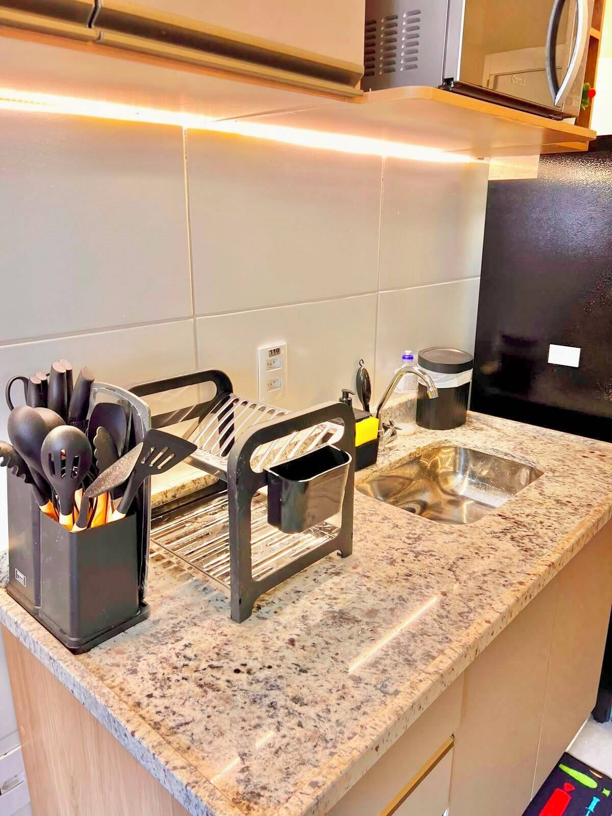 A kitchen with a granite countertop, a sink, a black utensil holder, and a stainless steel pot.