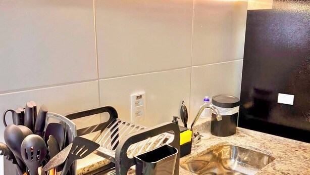 Una cocina con encimera de granito, un lavamanos, un recipiente negro para utensilios y una olla de acero inoxidable.