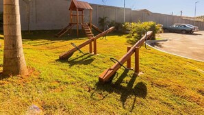 Un parque infantil con un tobogán y una estructura para escalar, una palmera y un coche estacionado al fondo.