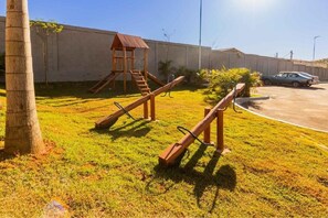 Un parque infantil con un tobogán y una estructura para escalar, una palmera y un coche estacionado al fondo.
