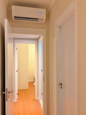 Un pasillo con un equipo de aire acondicionado instalado en la pared, suelo de madera y puertas blancas.