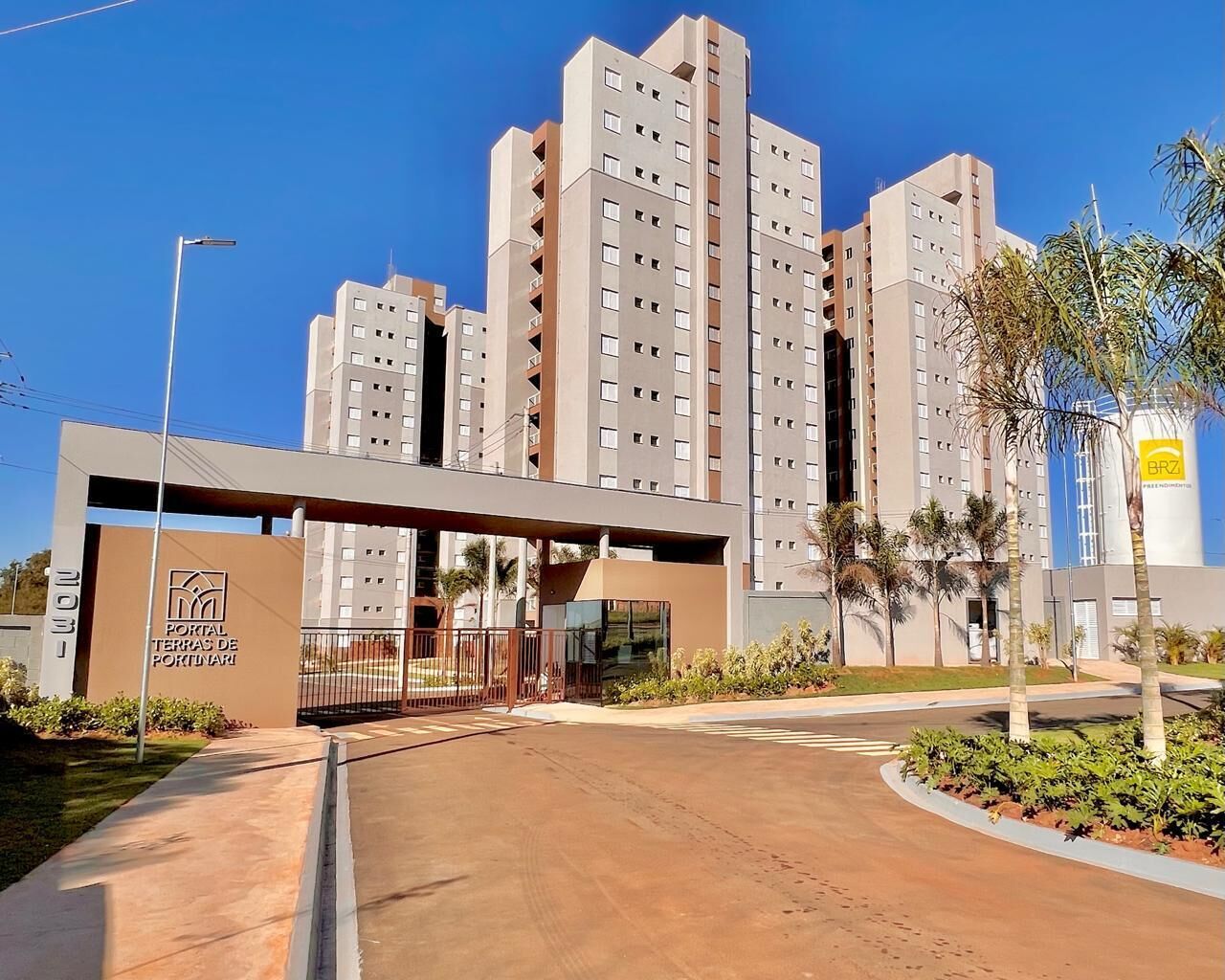 A modern apartment complex with multiple high-rise buildings, a gated entrance, and a clear sky.