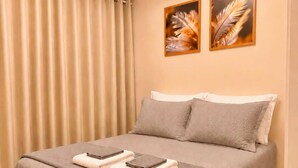 Una cama bien hecha con una colcha gris y almohadas, un par de toallas dobladas sobre la cama y dos piezas decorativas de plumas en la pared encima.