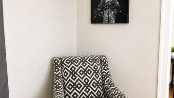 A corner room with a patterned armchair, a framed picture on the wall, and a wooden floor.