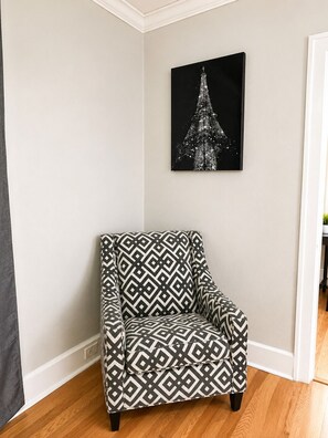 Habitación de esquina con un sillón estampado, un cuadro en la pared y piso de madera.