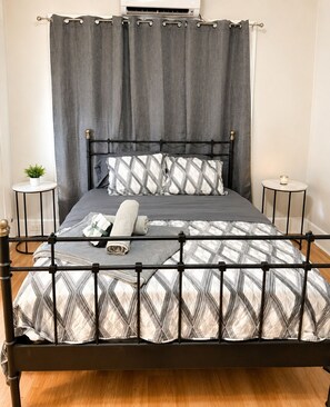 Una cama con estructura metálica, cortinas grises y ropa de cama estampada.