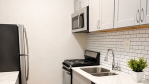 A compact kitchen with stainless steel appliances, white cabinets, a tiled backsplash, and a wooden floor. - Modern Downtown Studio - Walk to Toyota Center (Houston)