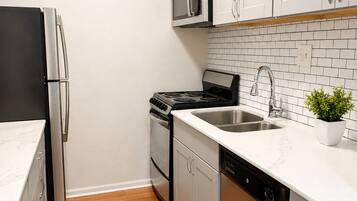 A compact kitchen with stainless steel appliances, white cabinets, a tiled backsplash, and a wooden floor.
