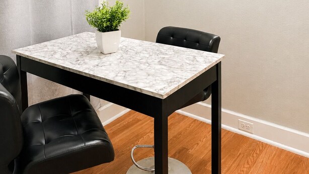 A small, modern room with a marble table, two black chairs, a potted plant, a round mirror, and a curtain. - Modern Downtown Studio - Walk to Toyota Center (Houston)